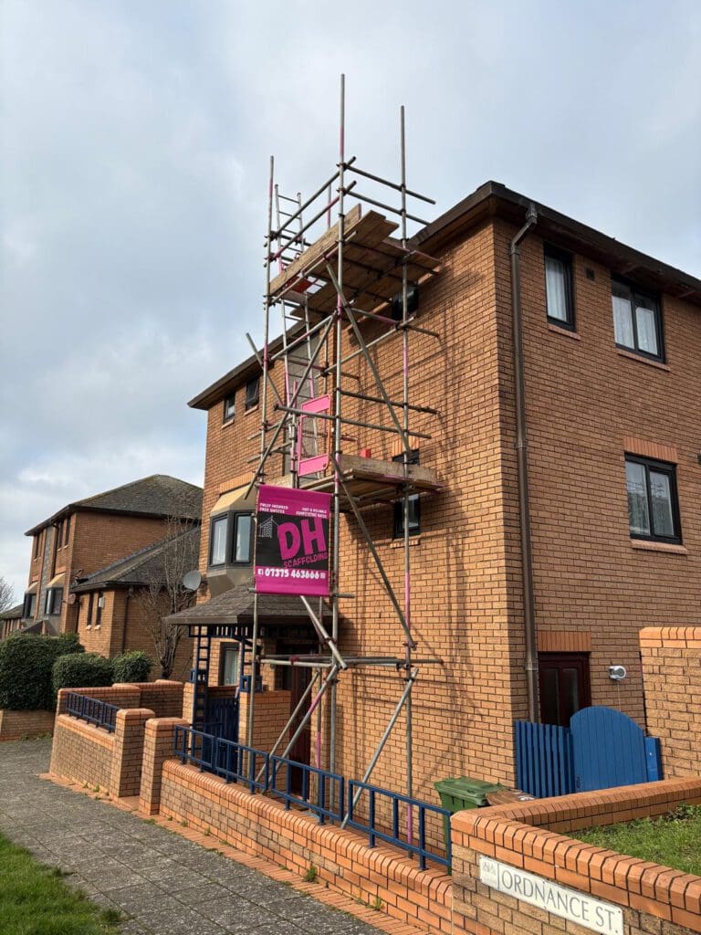 A three-story brick house with domestic scaffolding set up on the front, featuring a pink "DH" construction sign. The house has black window frames and is located on Ordnance Street, as shown by the street sign.